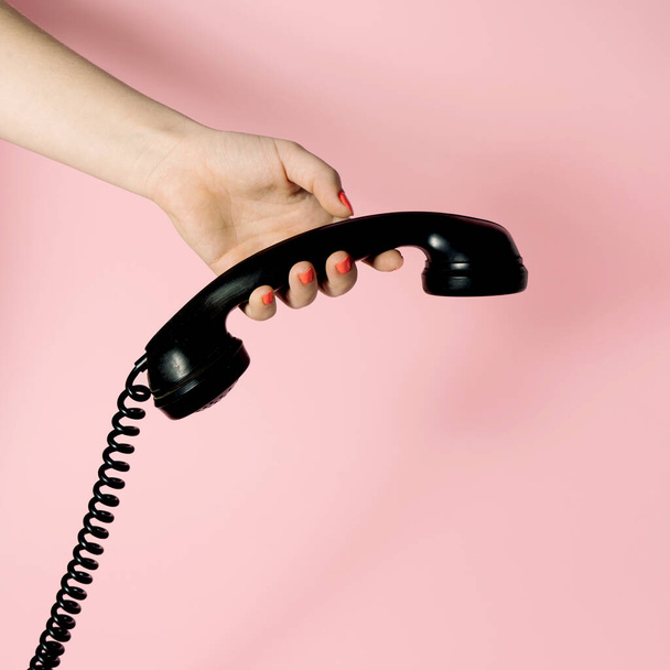 Visual artístico con la mano femenina sosteniendo audaz receptor de teléfono negro. Ambiente vintage sobre fondo pastel. Composición mínima. - Foto, Imagen