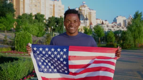 Retrato feliz Africano adulto masculino étnico preto fica no parque com bandeira dos EUA - Filmagem, Vídeo