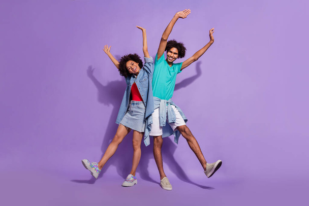 Full size photo of cool joyful dark skin couple raise hands smile enjoy isolated on purple color background - Zdjęcie, obraz