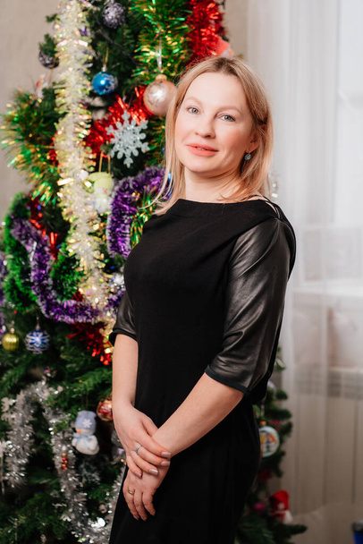 ελκυστική ξανθιά γυναίκα με μαύρο φόρεμα από το χριστουγεννιάτικο δέντρο. ελεύθερη ανύπαντρη γυναίκα - Φωτογραφία, εικόνα