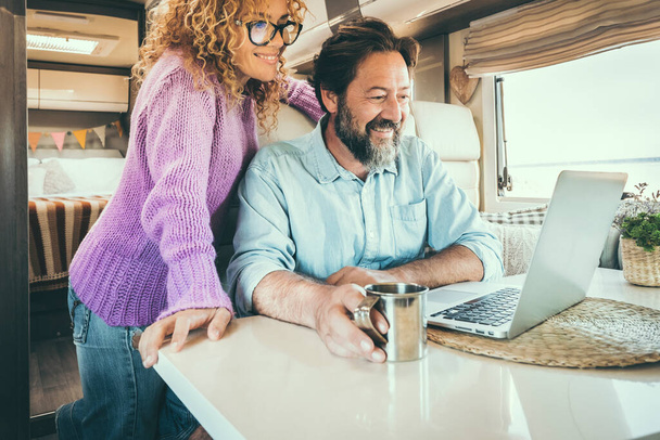 Modern travel couple enjoy connection technology using laptop inside a camper van home. Alternative office and house people lifestyle. Digital nomad smart working man and woman trip - Photo, Image