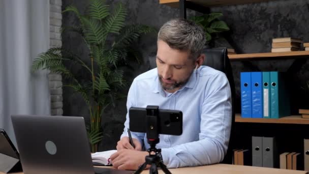 Man handelaar communiceert online laptop met investeerder, maakt notities in notebook - Video