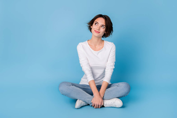 Photo of pretty dreamy woman wear white shirt sitting legs crossed looking empty space isolated blue color background - Valokuva, kuva