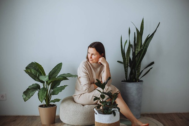Middle-aged woman sitting at home surrounded by domestic green plants - Foto, afbeelding