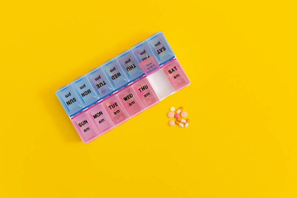 Daily pill box with medical pills on yellow background. - Foto, afbeelding