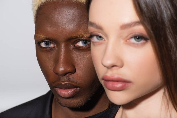 vista de cerca de joven pareja interracial mirando a la cámara aislada en gris - Foto, Imagen