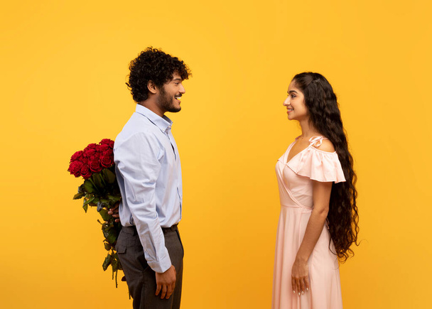 Αγαπώντας τον Ινδό που κρύβει λουλούδια για την αγαπημένη του πίσω από την πλάτη του, ο εραστής δίνει στη γυναίκα του τριαντάφυλλα για την Ημέρα του Αγίου Βαλεντίνου - Φωτογραφία, εικόνα