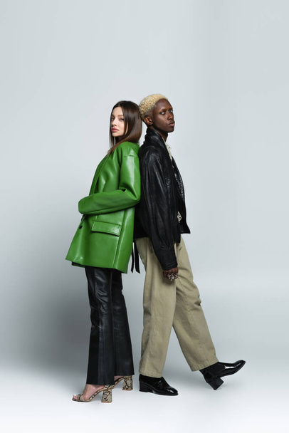 brunette woman and blonde african american man in trendy clothes standing back to back on grey - Foto, Imagem