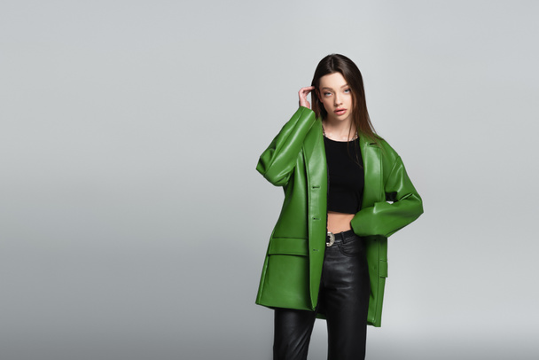 pretty woman in green jacket and black trousers standing with hand on waist isolated on grey - Photo, Image