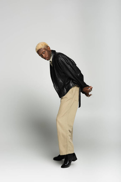 glamour african american man with bleached hair posing with hands behind back on grey - Foto, immagini