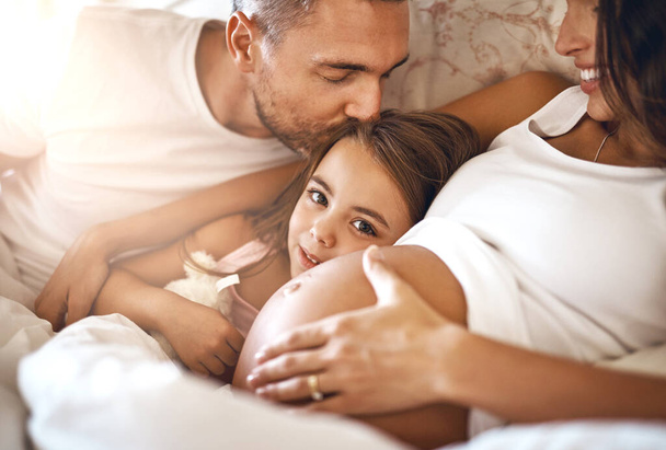 Van elég szeretet még egynek. Egy boldog kislányról, aki az ágyban fekszik az apjával és a terhes anyjával.. - Fotó, kép