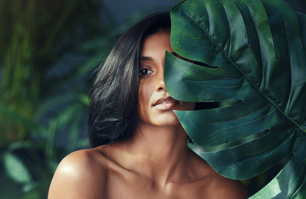 Shes just perfect. Studio shot of a beautiful young woman holding a monstera leaf against her face. - Фото, изображение