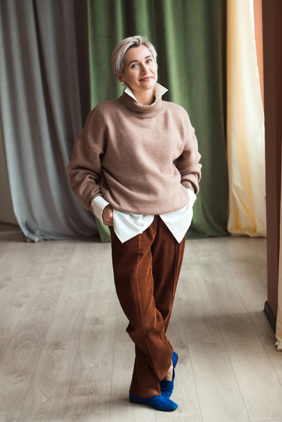 fashion woman in brown oversize sweater and trousers standing in modern work place or office - Foto, afbeelding