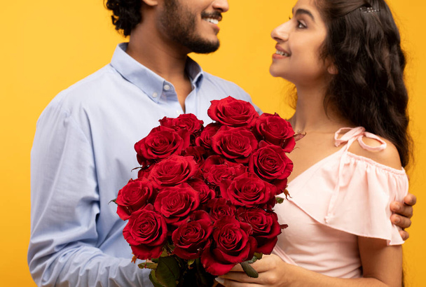 Fecha romántica de vacaciones. Jóvenes cónyuges indios abrazando y sosteniendo ramo de flores sonriendo el uno al otro, primer plano - Foto, imagen
