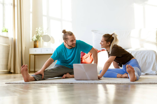 Молодая пара выбирает онлайн растяжения или йоги тренировки программы дома перед монитором ноутбука. Концепция здорового образа жизни и поддержания хорошей физической формы. - Фото, изображение