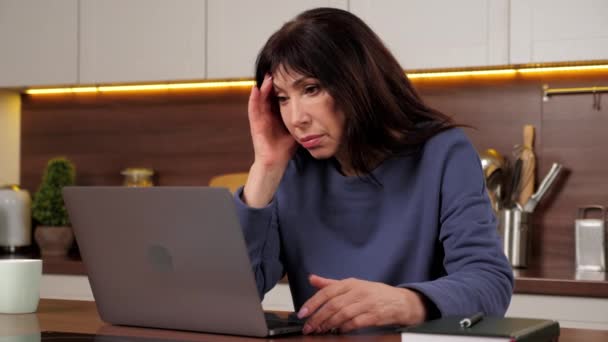 Mujer agotada usa laptop sintiéndose preocupada leyendo malas noticias en las redes sociales - Metraje, vídeo