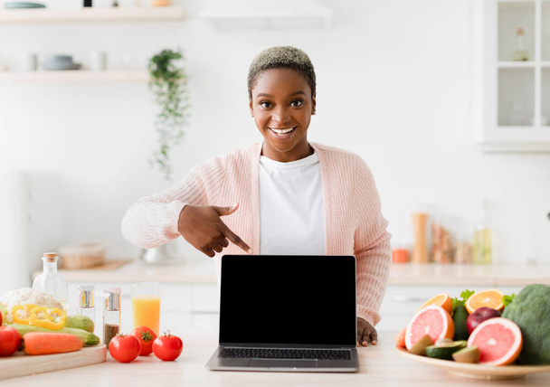 Happy glad excited young black female blogger points finger at pc with empty screen - Фото, изображение
