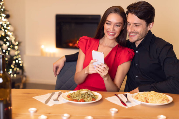 Couple souriant utilisant un téléphone portable pendant le dîner - Photo, image