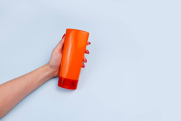 Markenloses orangefarbenes Shampoo und Conditioner-Flasche für Branding und Etikett und weibliche Hand auf blauem Hintergrund. Minimalismus, Attrappe - Foto, Bild