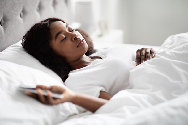 Donna nera infelice sdraiata sul letto, con il cellulare in mano - Foto, immagini