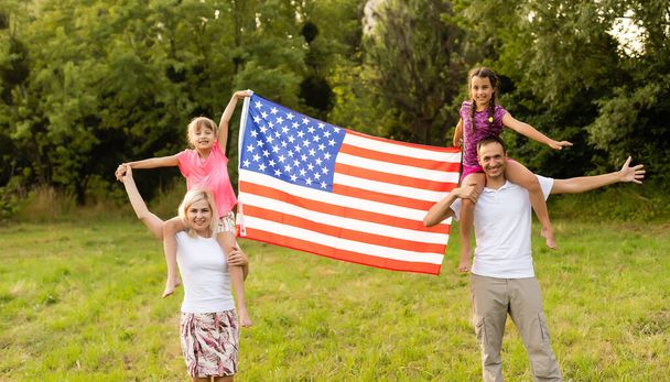 Ευτυχισμένη οικογένεια στο πεδίο με τις ΗΠΑ, αμερικανική σημαία στην πλάτη. - Φωτογραφία, εικόνα