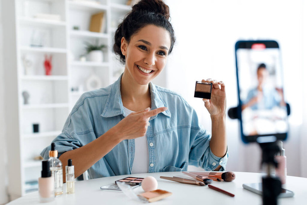 Lady Blogger mostrando el producto de maquillaje al teléfono haciendo video en interiores - Foto, imagen