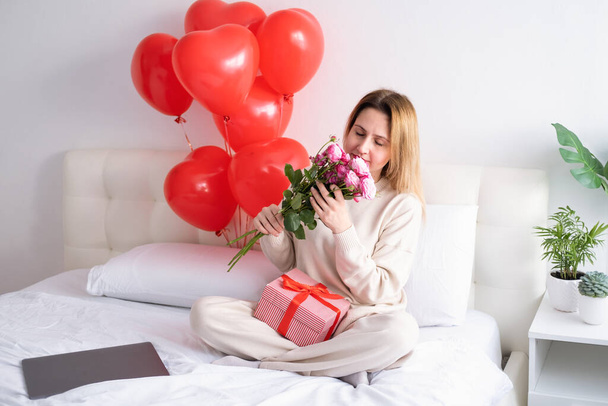 Beautiful women holding bouquet of pink roses on bed celebrating Valentine day - Foto, Imagen
