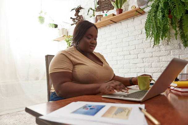 Чорна жінка друкує і дивиться на ноутбук на роботі
 - Фото, зображення