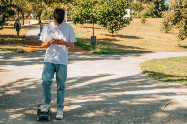 adolescente con teléfono móvil y monopatín en la calle - Foto, Imagen