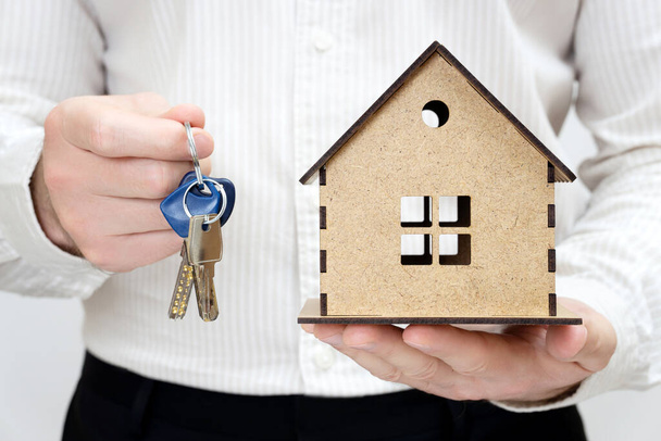 Man holding keys and a miniature wooden house model in hands. Get the keys day concept. - Foto, Bild