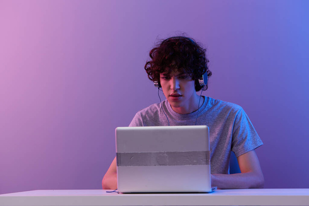 krullende man zitten aan de tafel gaming laptop geïsoleerde achtergrond - Foto, afbeelding