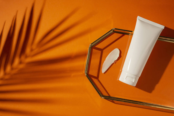 Plastic witte tube voor lotion en het uiterlijk van de textuur van de crème in glazen lade op oranje bacground. Huidverzorging of zonnebrandcrème cosmetisch in het bovenste uitzicht. Schoonheidsconcept voor gezichtsverzorging - Foto, afbeelding