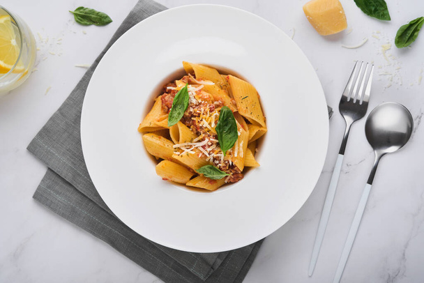 Bolognese Penne Pasta. Tasty appetizing classic italian penne pasta with parmesan cheese, basil and Bolognese sauce in white plate on plate on stone table. Traditional dish of Italian cuisine Top view - Foto, Bild