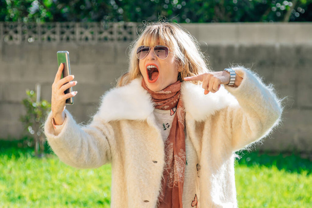 mulher usando telefone celular ao ar livre com expressão animada de emoção e surpresa - Foto, Imagem