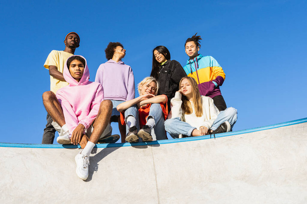 Multicultural group of young friends bonding outdoors and having fun - Stylish cool teens gathering at urban skate park - Foto, imagen