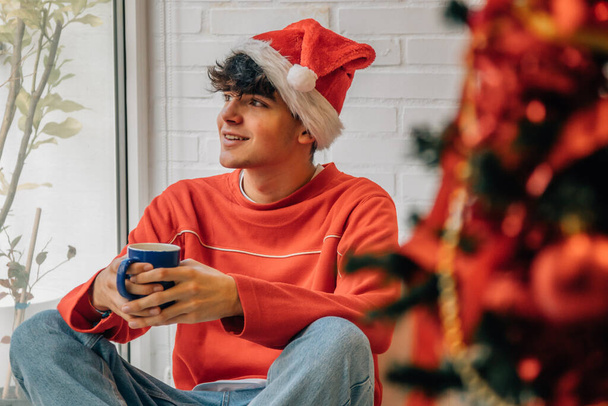 έφηβος στο σπίτι με χριστουγεννιάτικο δέντρο και κύπελλο - Φωτογραφία, εικόνα