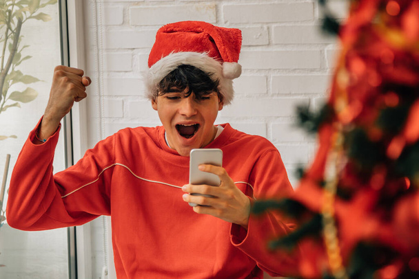 クリスマスに家でお祝いする携帯電話を持つ若い十代の若者 - 写真・画像