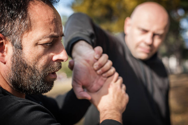 Kapap instructor demonstrates street fighting self defense technique against holds and grabs with his student - Photo, image