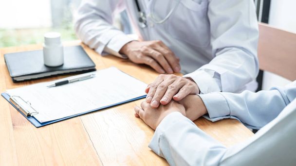 Male doctor hold hand patient to encourage and explaining treatment after writing prescription on clipboard and discussion the result of the examination of the illness to patient in clinic - Foto, Imagen