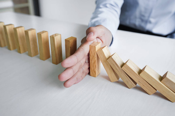 Risk and strategy in business, Close up of business woman hand stopping wooden block between three way from falling in the line of domino. - 写真・画像