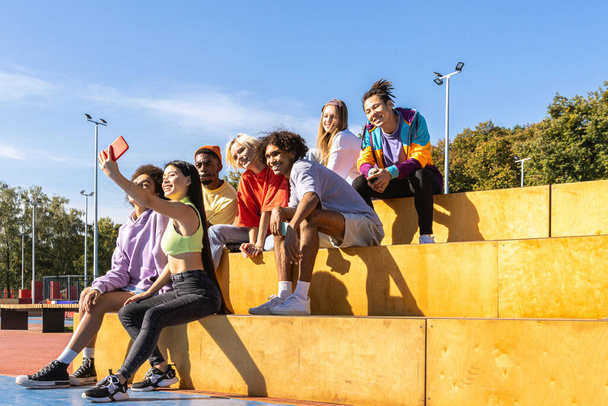 Multicultural group of young friends bonding outdoors and having fun - Stylish cool teens gathering at urban skate park - Фото, изображение