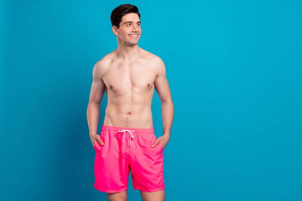 Photo of cheerful positive dreamy guy look empty space wear swimwear shorts isolated blue color background - Foto, immagini