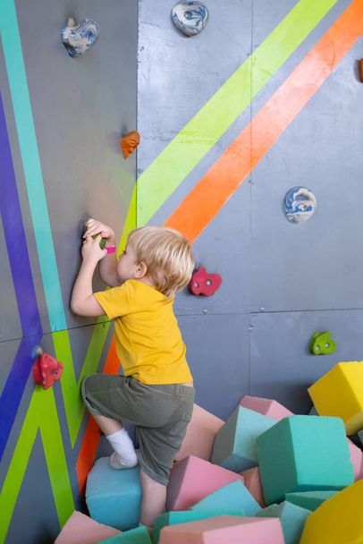 Malý roztomilý chlapec je lezení na svislé zdi vnitřní v zábavním parku - Fotografie, Obrázek