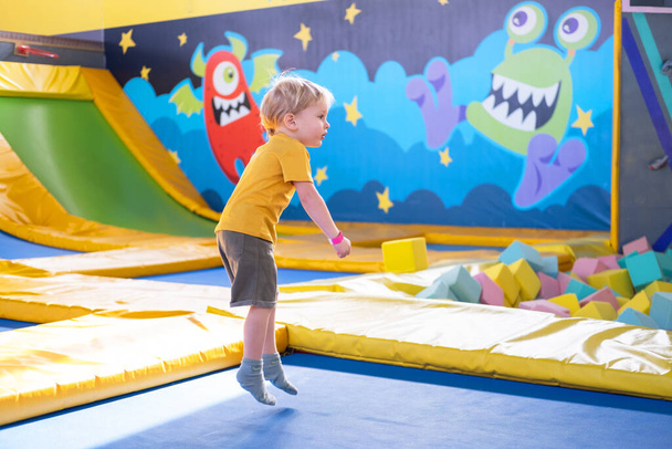 cute blond little boy jumps in a trampoline park, children activity - Fotó, kép