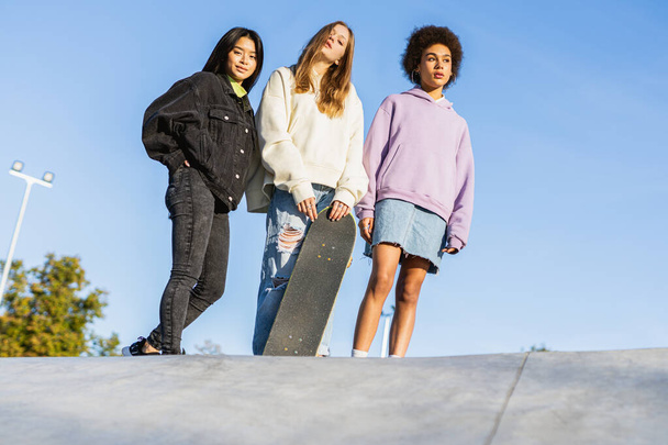Мультикультурная группа молодых друзей, объединяющихся на свежем воздухе и веселящихся - стильные крутые подростки собираются в городском скейт-парке - Фото, изображение