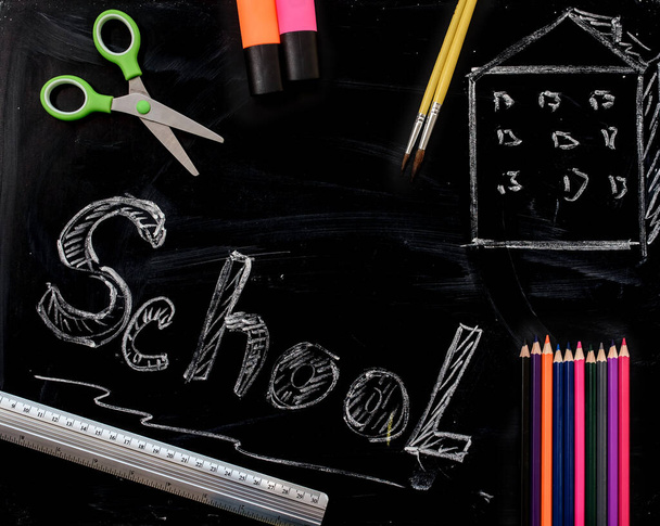 School supplies on a blackboard with school inscription. Back to school concept, markers, crayons, scissors, pen, brushes on blackboard. Copy space for you text - 写真・画像