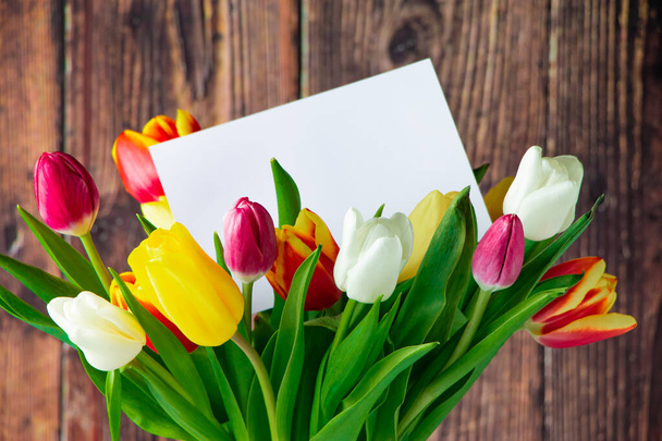 Kleurrijke tulpen boeket en wenskaart op houten achtergrond. Vakantie cadeau. Voorjaarssymbool, plaats voor tekst. - Foto, afbeelding