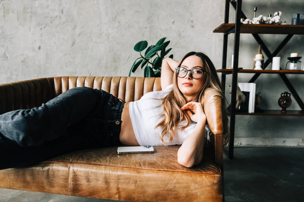 Young calm caucasian woman relaxing, lying on the sofa in modern living room, lazy happy woman resting at home. - Foto, Bild