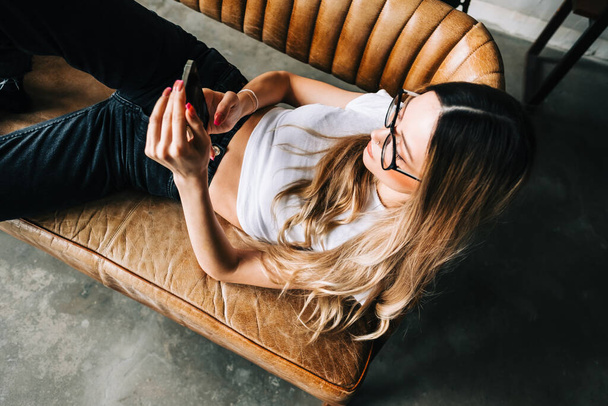 Young caucasian woman using mobile phone while resting on a sofa at home.  - Fotoğraf, Görsel