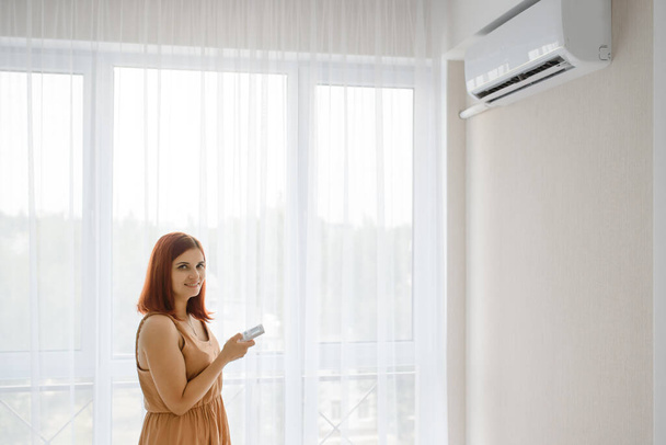 Giovane bella donna nel suo appartamento bianco accende il condizionatore d'aria e gode il fresco. Lotta con concetto di calore - Foto, immagini
